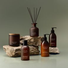 A candle, reed diffuser, room spray and ath body products from the M&S Apothecary range displayed on stacked rocks