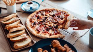 Pizza, garlic bread and chicken winds, processed foods sitting on table