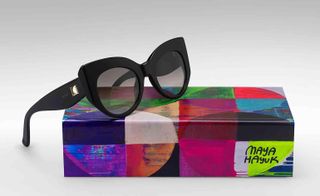Black, "cat eye" sunglasses sit on a box designed by Maya Hayuk. The design on the box is made out of colorful geometrical shapes.