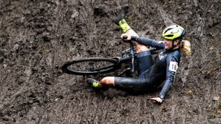 Cyclocross rider slipping down muddy slope with her bike