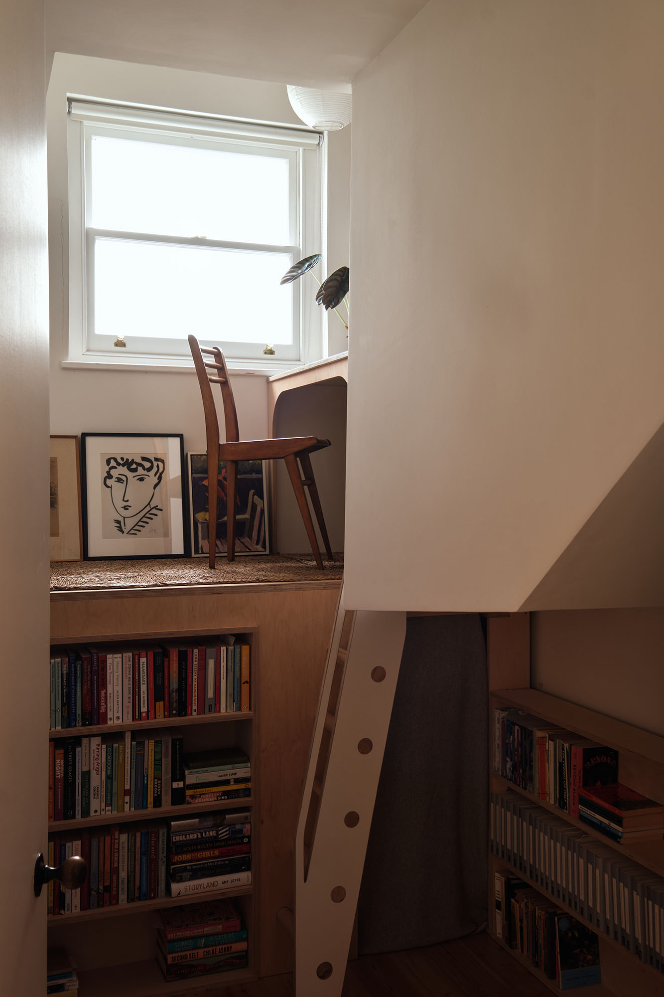 Interiors of a beautifully designed, spacious home with wooden floors, neutral decor, and lots of colorful accessories and furniture, including thriving plants and a golden-glowing paper lamp.