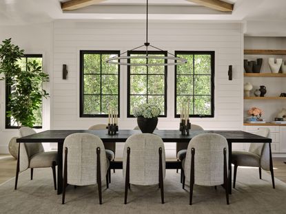dining room with black table and white upholstered chairs with black steel framed windows and tree views beyond