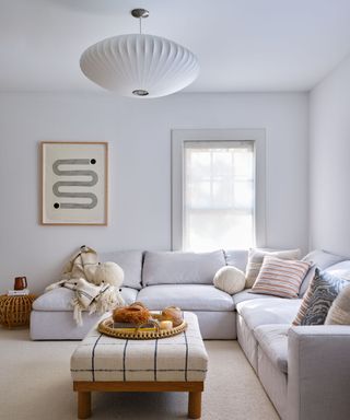 neutral living room with white walls and light gray sectional sofa and beige ottoman