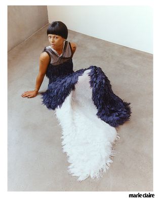 Actress Myha'la Herrold sitting on a concrete floor in a blue and white feather dress