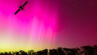 the silhouette of a satellite against a colorful aurora in the sky