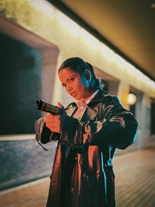 A model in a trench coat aiming a gun