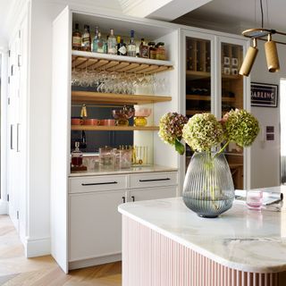 white drinks cabinet with a countertop kitchen island opposite with a vase of flowers