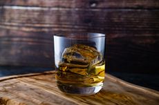 A glass of bourbon with ice on top of a barrel