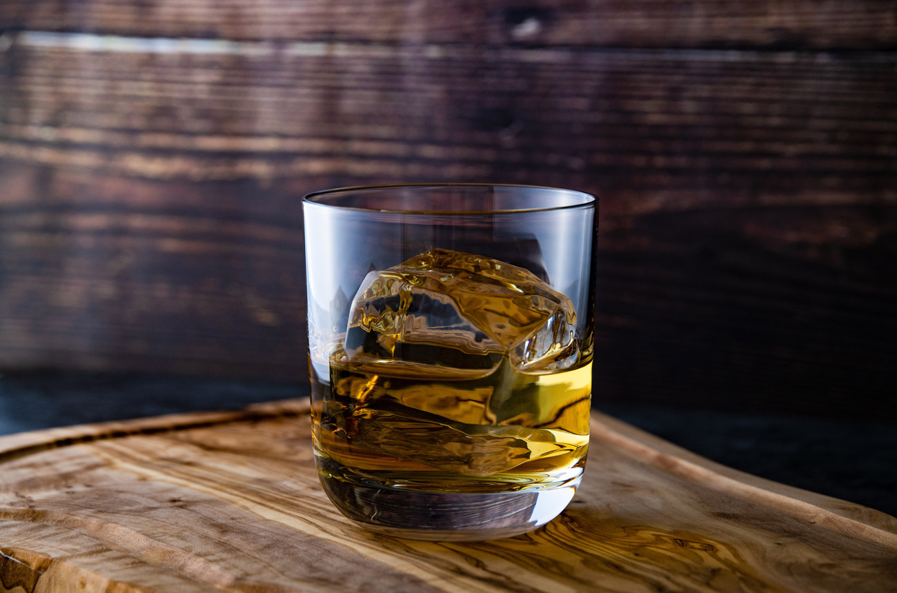 A glass of bourbon with ice on top of a barrel