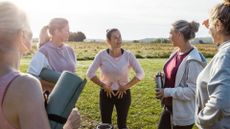 Women learning how to practise self-care outdoors with yoga mats and instructor demonstrating deep breathing techniques