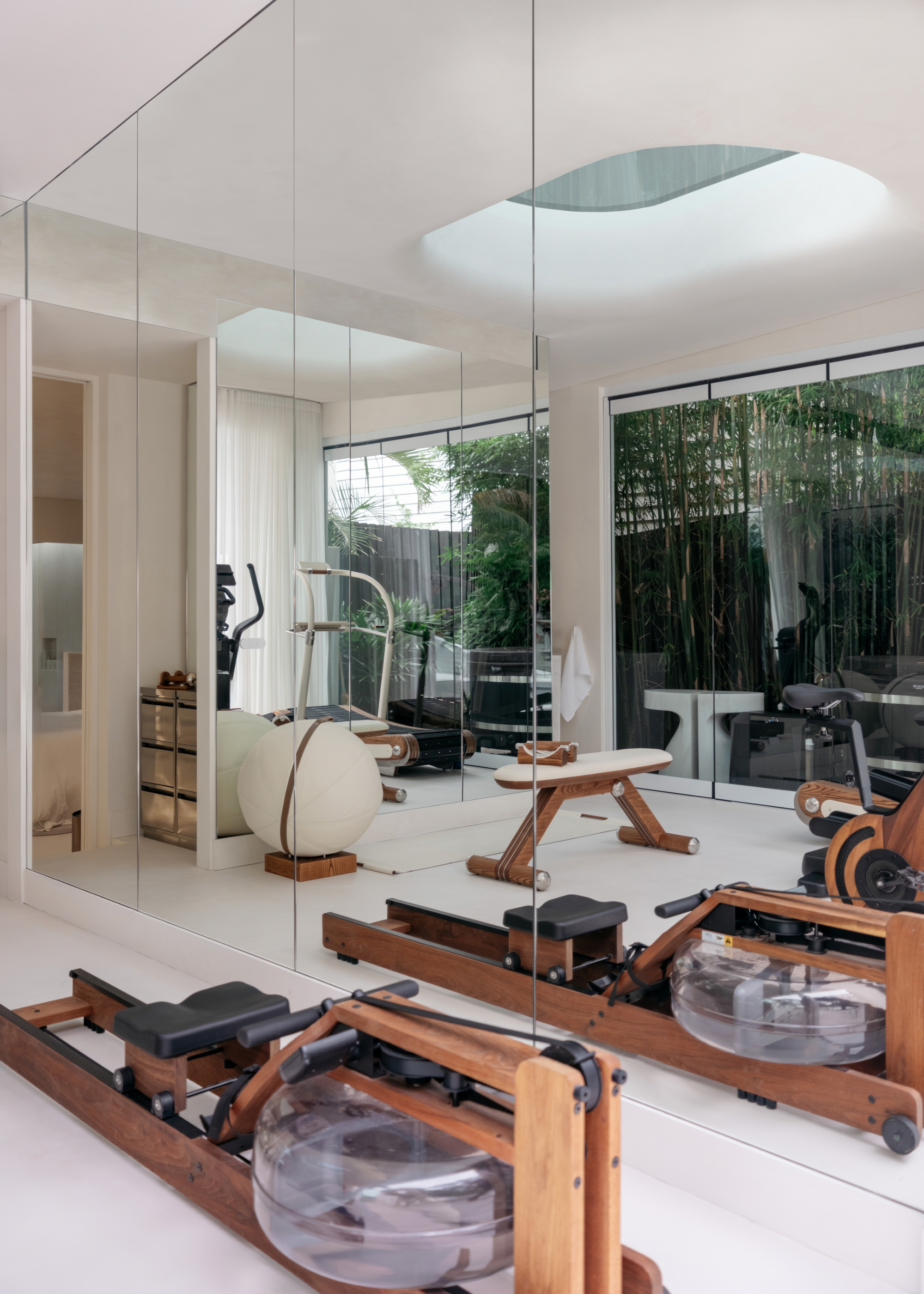 A workout space with a wood reformer machine, a boucle gym ball, and a minimalist bench reflected in the mirror