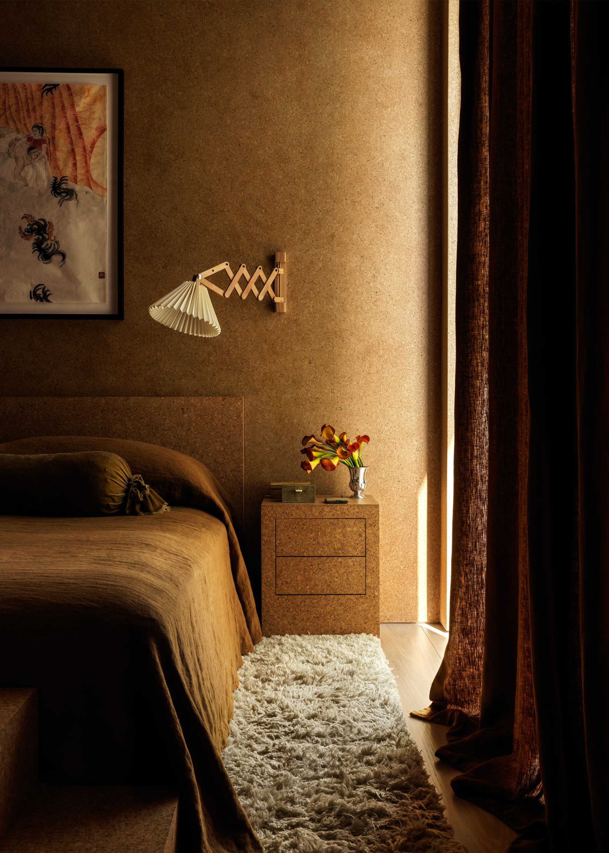 A bedroom with a fluffy carpet, ochre bedding and a wall-installed lamp