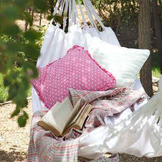 White cotton hammock with pink and white cushions and checked throw