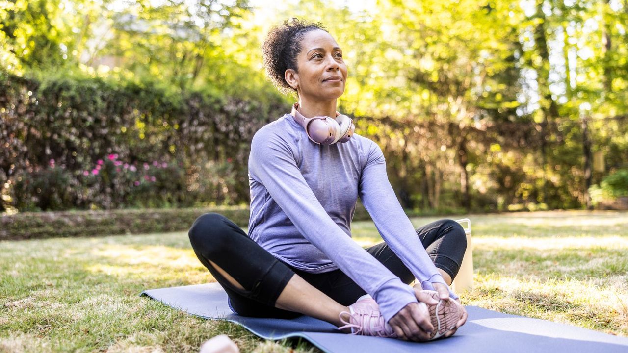 Woman doing glute stretches sitting down on yoga mat in sunny garden