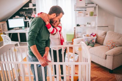 Young couple, who is expecting a baby, assembling a baby crib in their living room