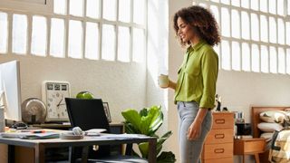 Woman standing up and walking over to her desk in the office after eating, carrying mug