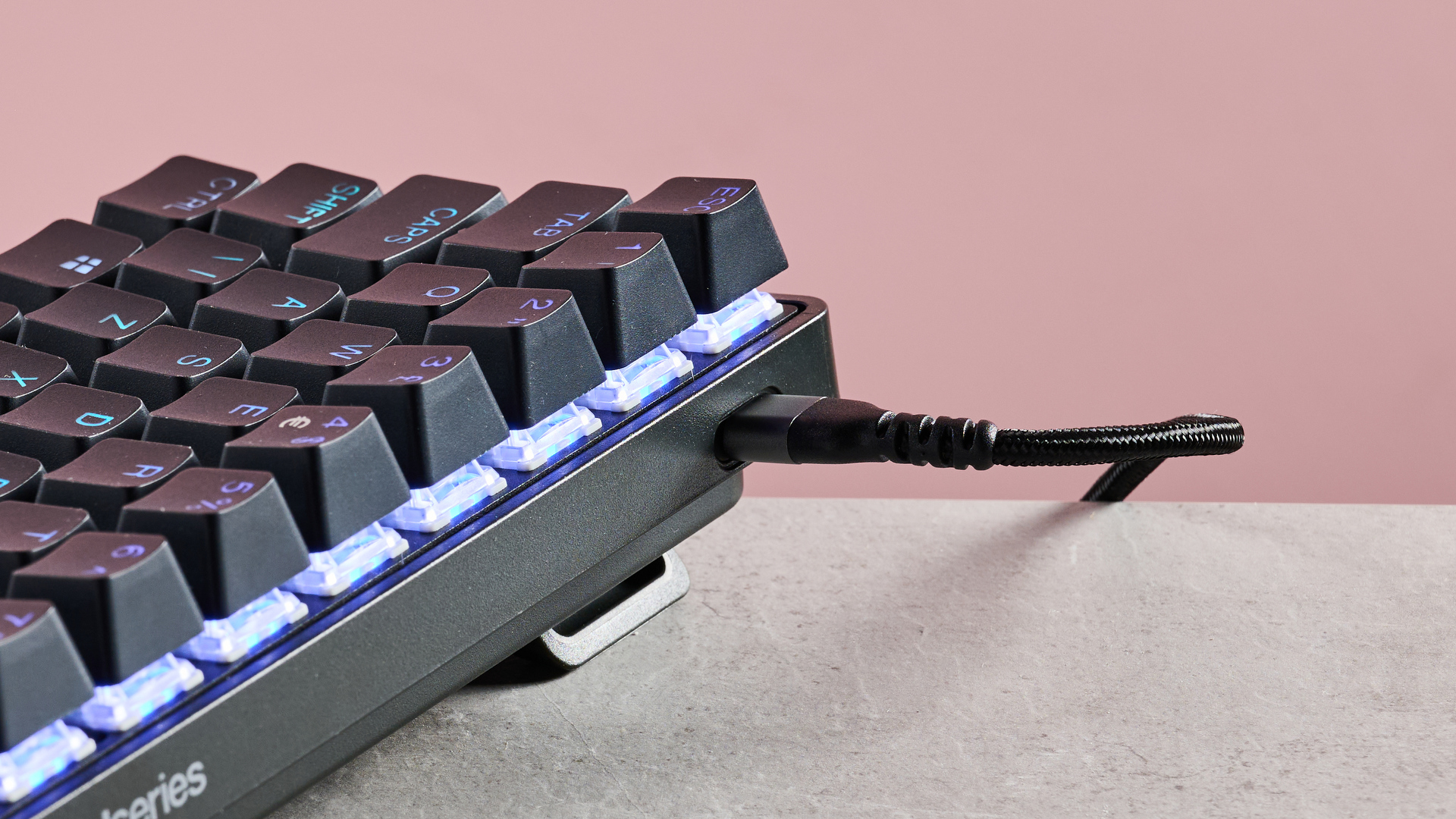 Close-up of USB-C cable connected to SteelSeries Apex Pro Mini, on desk with pink background