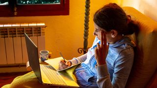 A woman looking at her laptop and taking notes in bed at night time