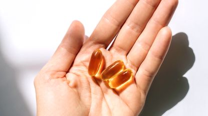 The palm of a hand holds three Omega-3 supplement capsules