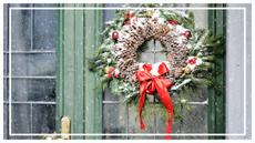 A traditional wreath hanging on an imposing green front door while snow falls
