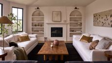 a large neutral wabi sabi living room with arched bookcases, linen sofas and warm wooden coffee table