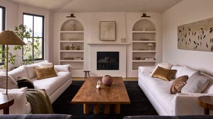 a large neutral wabi sabi living room with arched bookcases, linen sofas and warm wooden coffee table