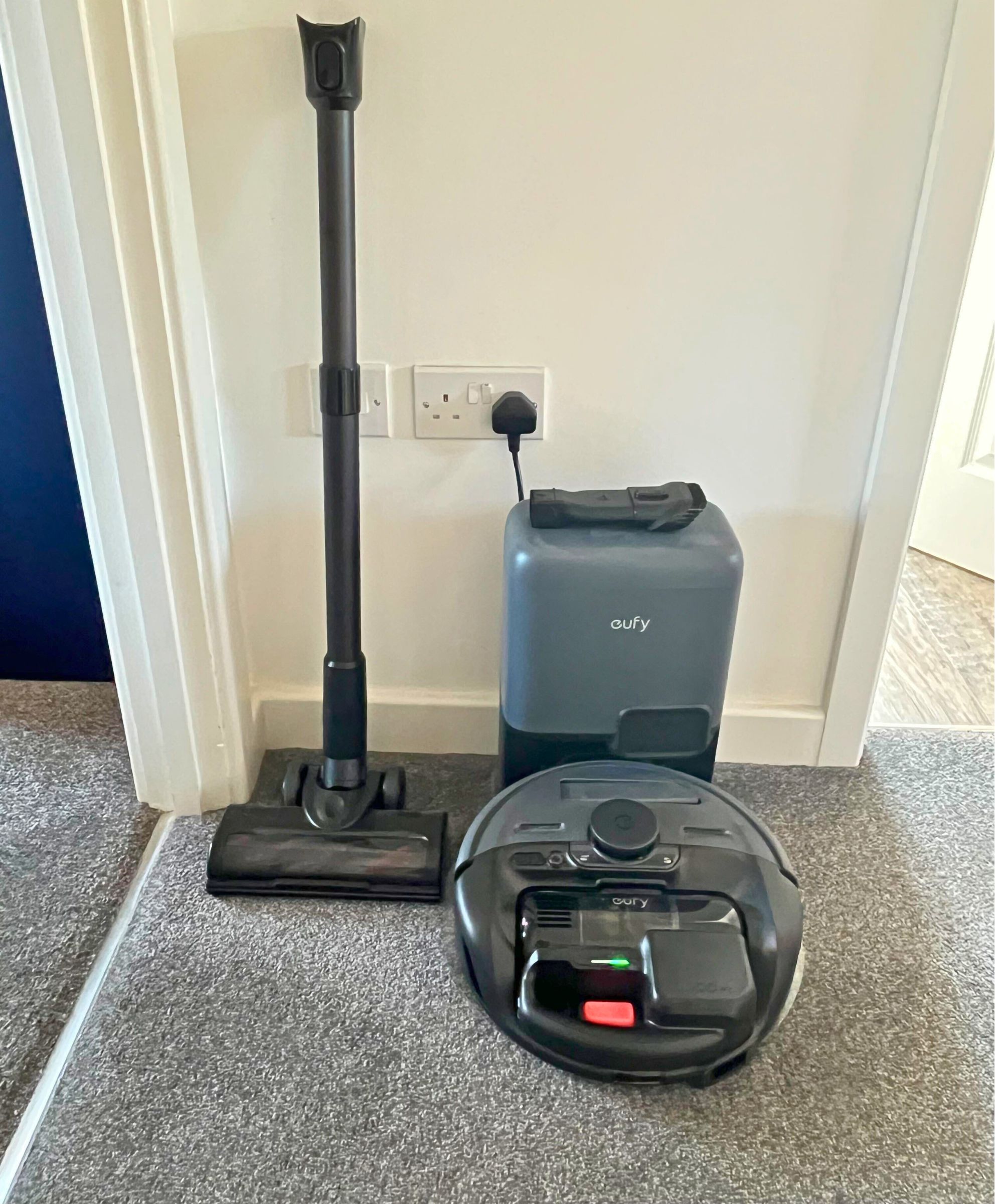 eufy E20 vacuum in small hallway with stick and floorhead leaning against the wall, with the robot docked in the small base station