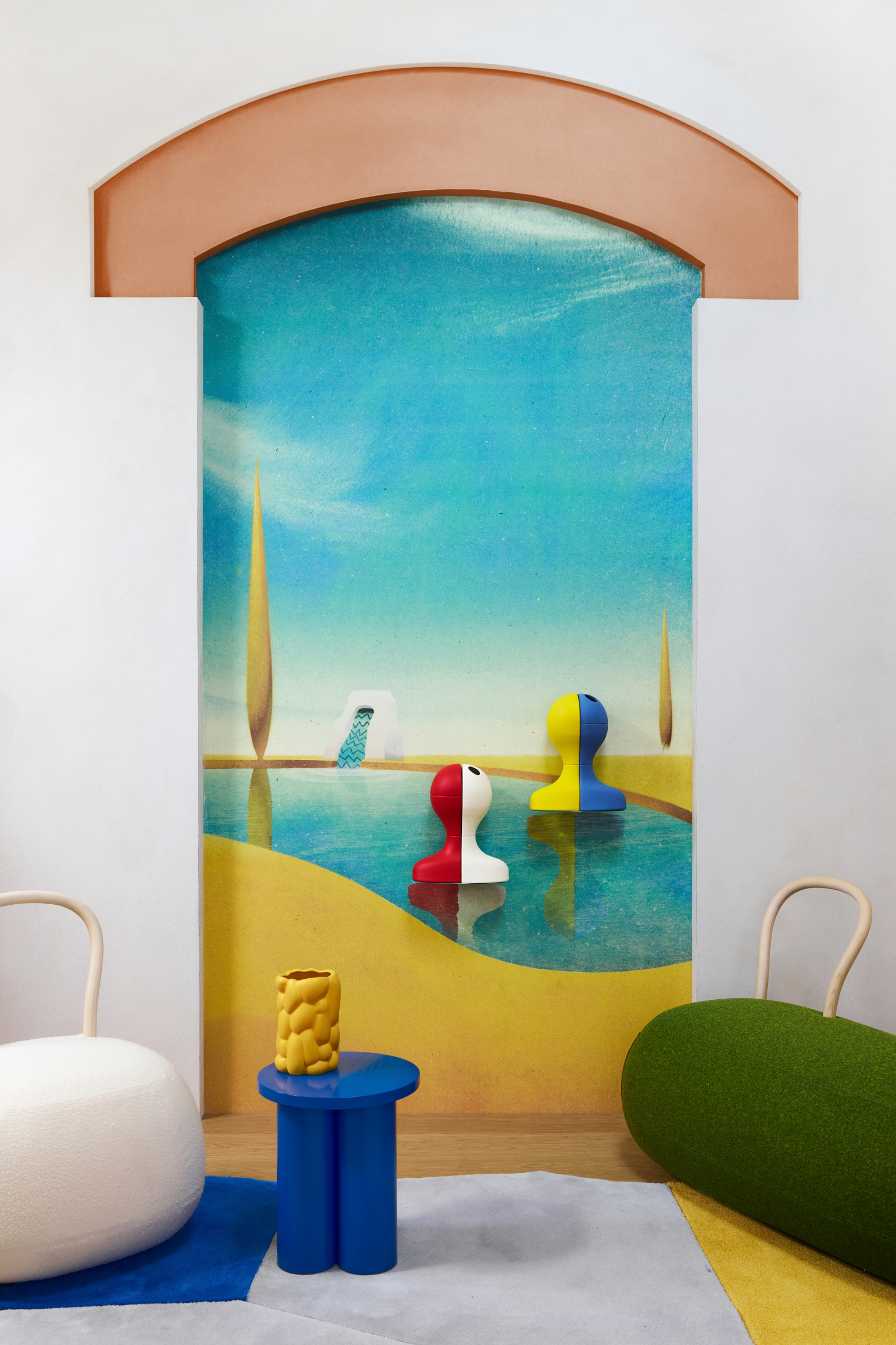 A mural of an oasis with a terracotta arch and two-toned wall vases. Also pictured are Yum Yum seats from Opinion Ciatti and a blue stool with a yellow textured vase