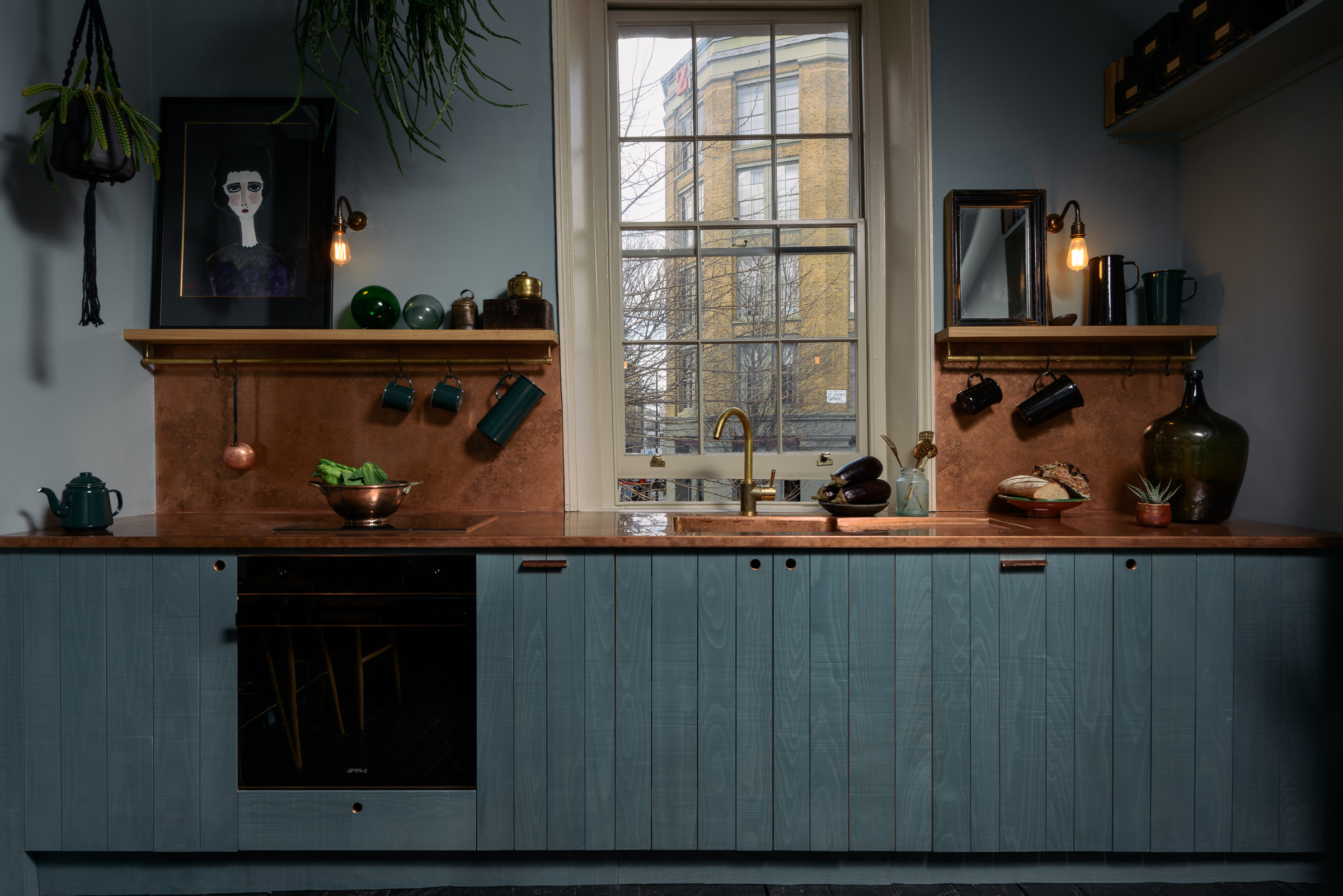 A single wall blue and copper kitchen with a window half way