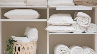 linen closet full of white bedding including duvet, pillows, sheets and towels