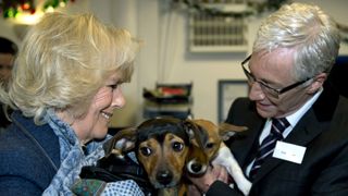 Camilla, Duchess of Cornwall stands next to television presenter Paul O'Grady while holding her two adopted dogs Bluebell and Beth