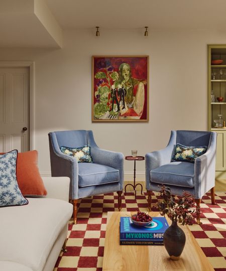 Beige living room with red and cream checked rug, cream sofa and blue accent chairs.