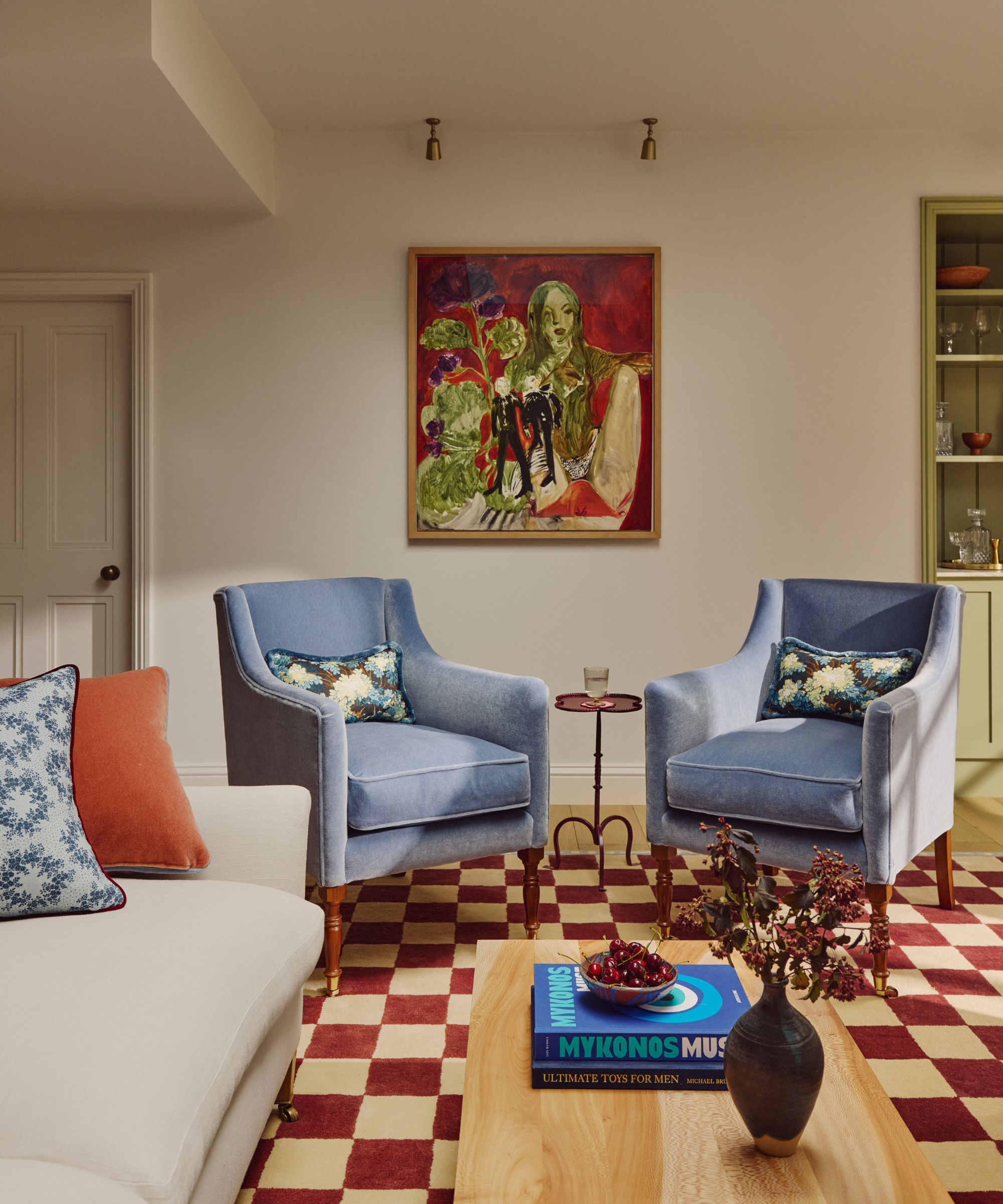 Beige living room with red and cream checked rug, cream sofa and blue accent chairs.