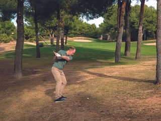 Golf Monthly Top 50 Coach John Howells hitting a shot from a difficult lie in the trees