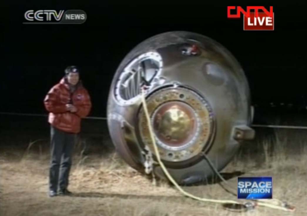 A CNTV reporter stands next to China&#039;s Shenzhou 8 space capsule on Nov. 17, 2011 after the unmanned spacecraft landed in inner Mongolia after a nearly two-week mission that successfully performed China&#039;s first space dockings in orbit.