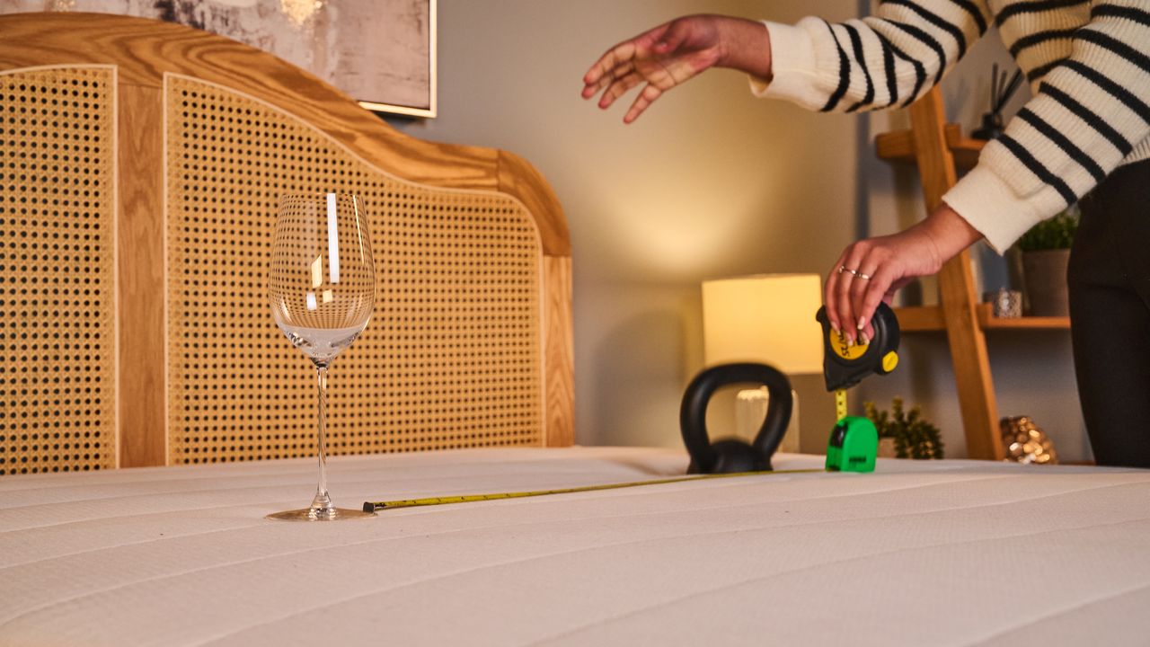A wine glass rests on top of the Helix Twilight Mattress. A tape measure marks 25 inches away, where a person drops a weight onto the mattress to test motion isolation