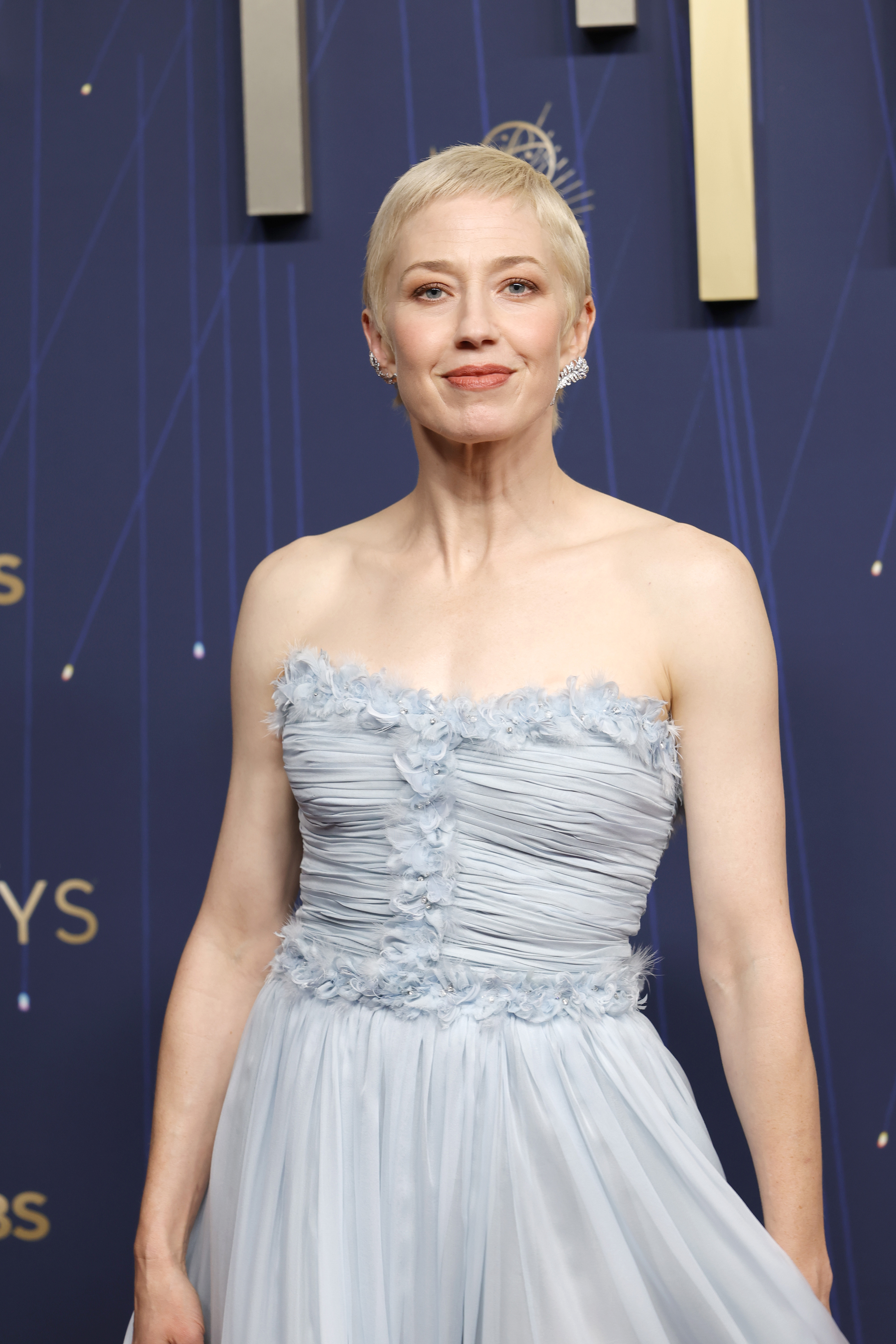 a woman with short, blonde hair wearing a strapless, light blue gown posing in front of a navy blue background