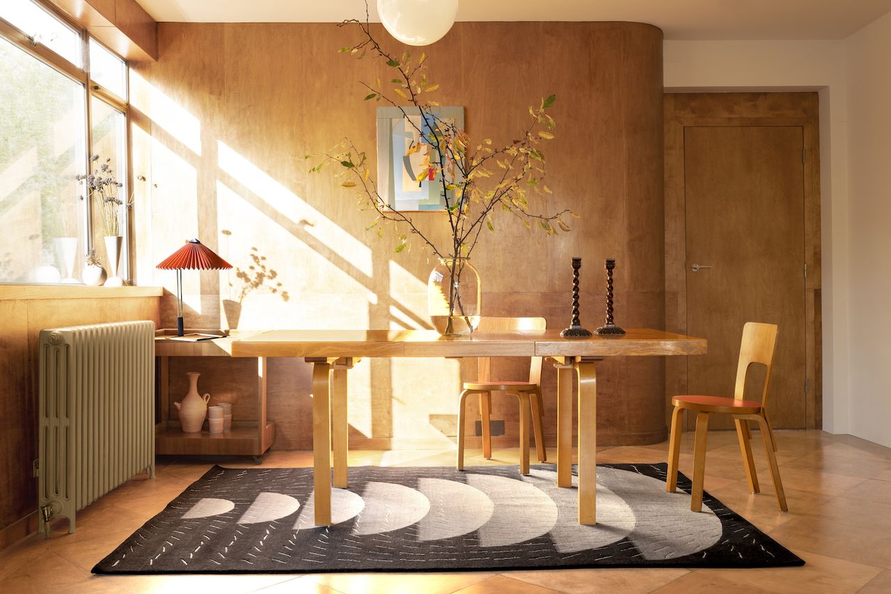 A dining room filled with light, with a table and dark coloured rug