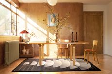 A dining room filled with light, with a table and dark coloured rug
