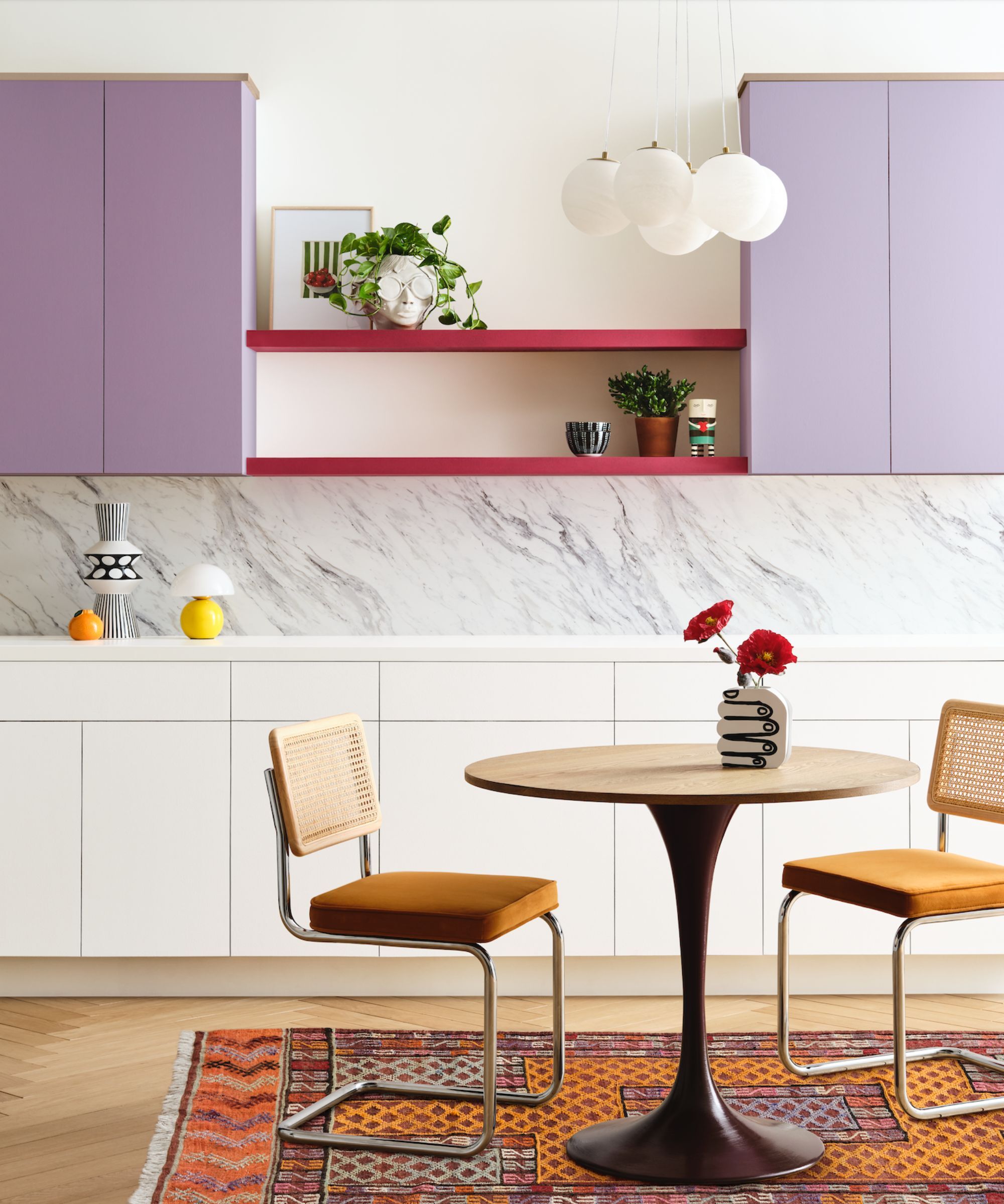 A modern kitchen with white lower cabinets and purple upper cabinets and a small bistro table with two chairs