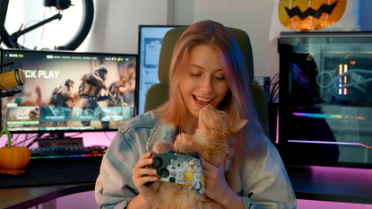 Call of Duty content creator NoisyButters holding cat and Scuf Valor Pro controller with PC setup in backdrop