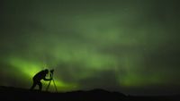 silhouette of photographer shooting aurora