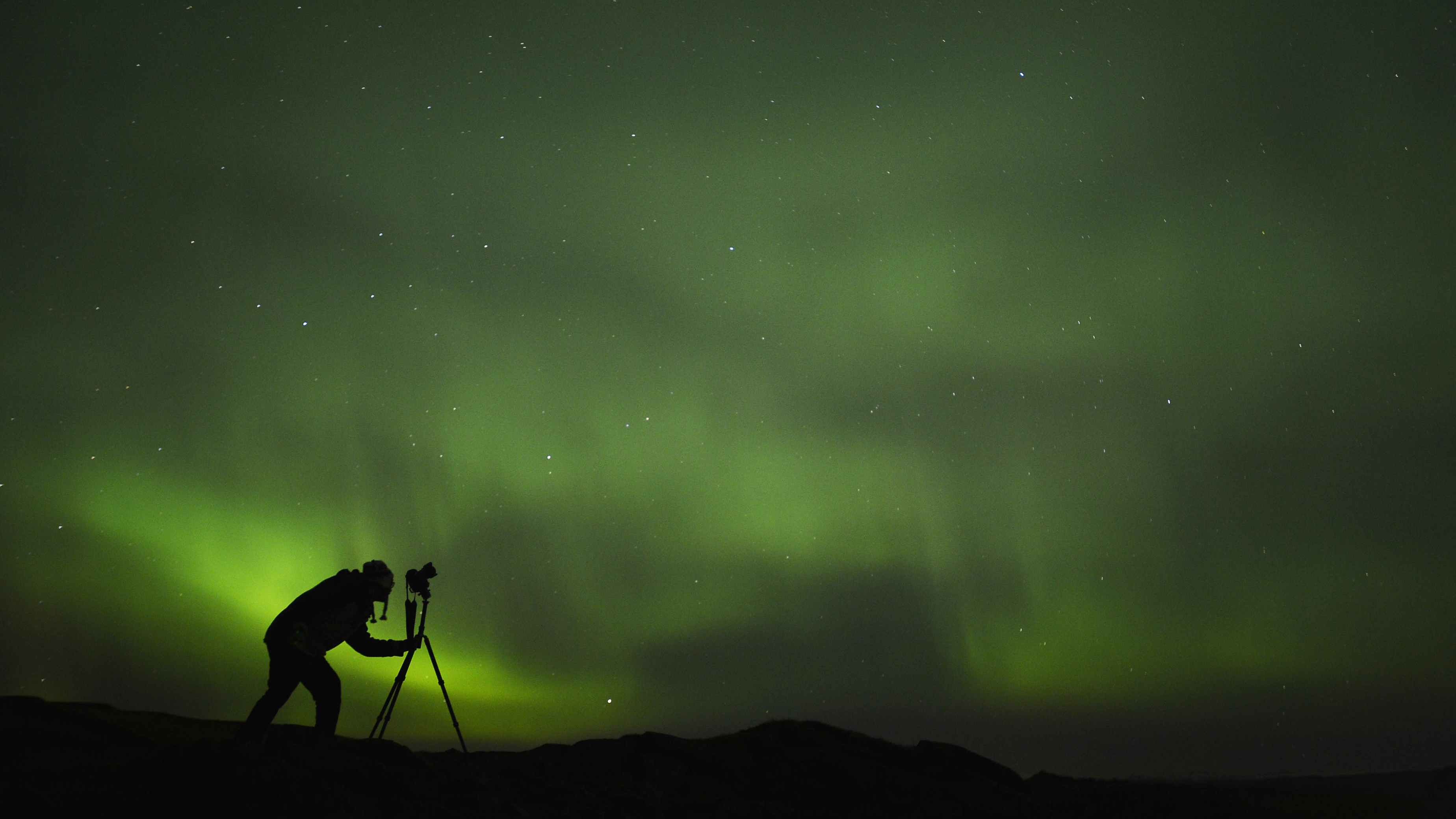 silhouette of photographer shooting aurora
