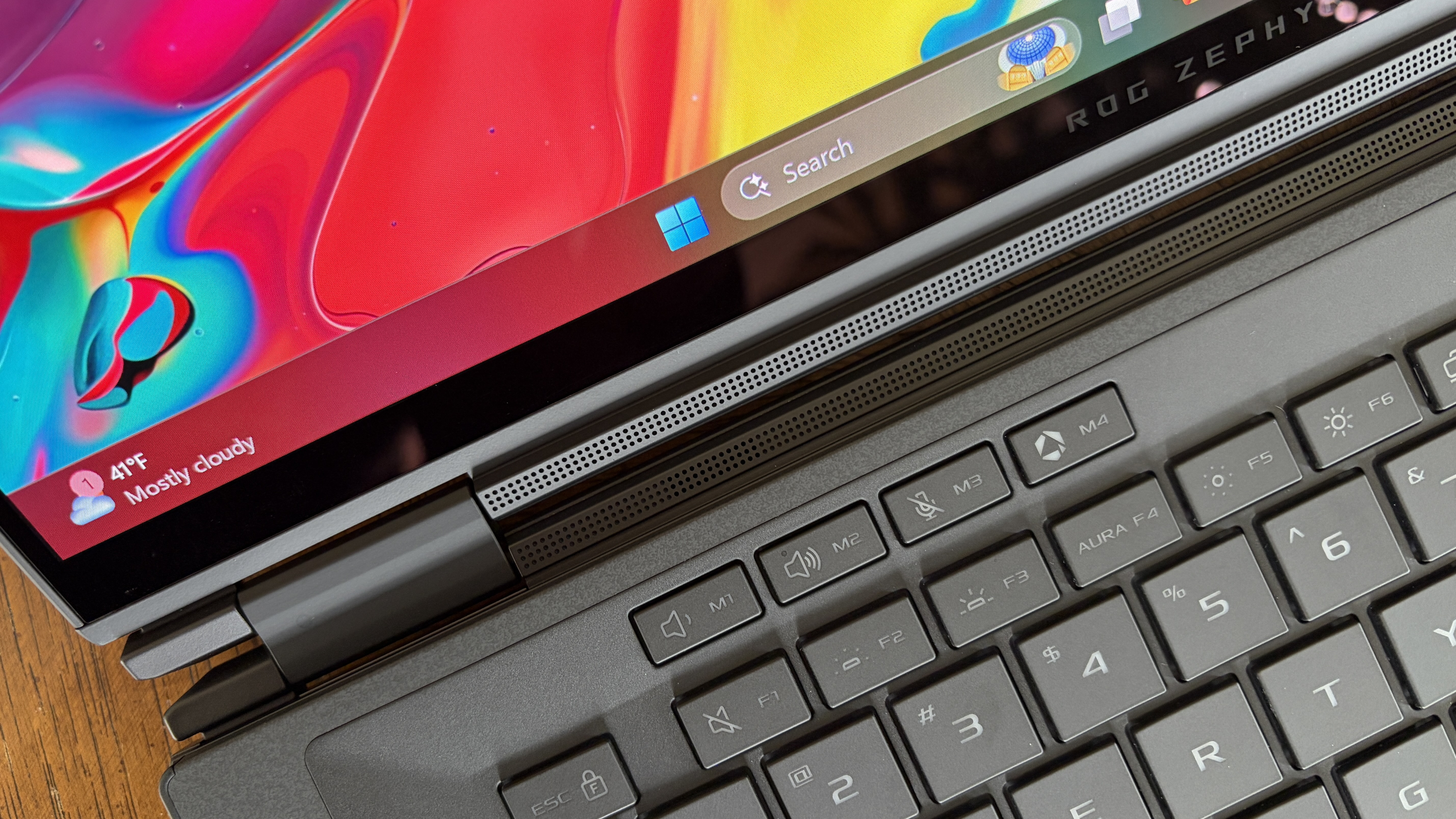 A close-up of a laptop displaying a colorful screen with swirling colors. The keyboard and part of the metal hinge are visible. The taskbar shows a partly cloudy weather icon and a temperature of 41&amp;deg;F. The overall tone is vibrant and modern.