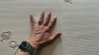 A hand rests on the surface of the Saatva Contour5 Mattress, testing the pressure relief