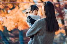 Woman with long black hair holding toddler in arms with autumn backdrop