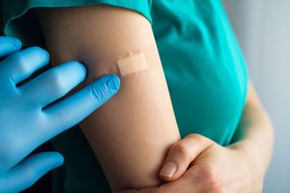 A doctor or health care professional applies a patch or adhesive bandage to a young woman after vaccination or injection of medication.