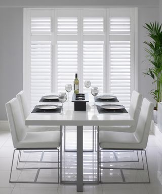 Minimalist white dining room with clean lines, and white full height window shutters.