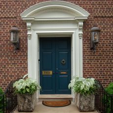 A double front door painted in Farrow & Ball's Hague Blue with two large planters in front of it 
