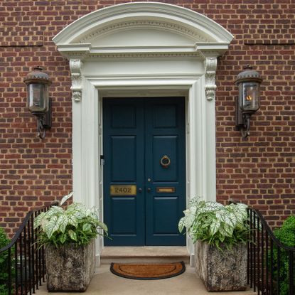 A double front door painted in Farrow & Ball's Hague Blue with two large planters in front of it